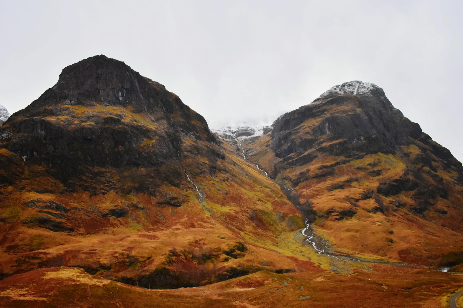Walkers on the West Highland Way descending toward Glen Coe, with the trail winding across open moorland and mountains behind